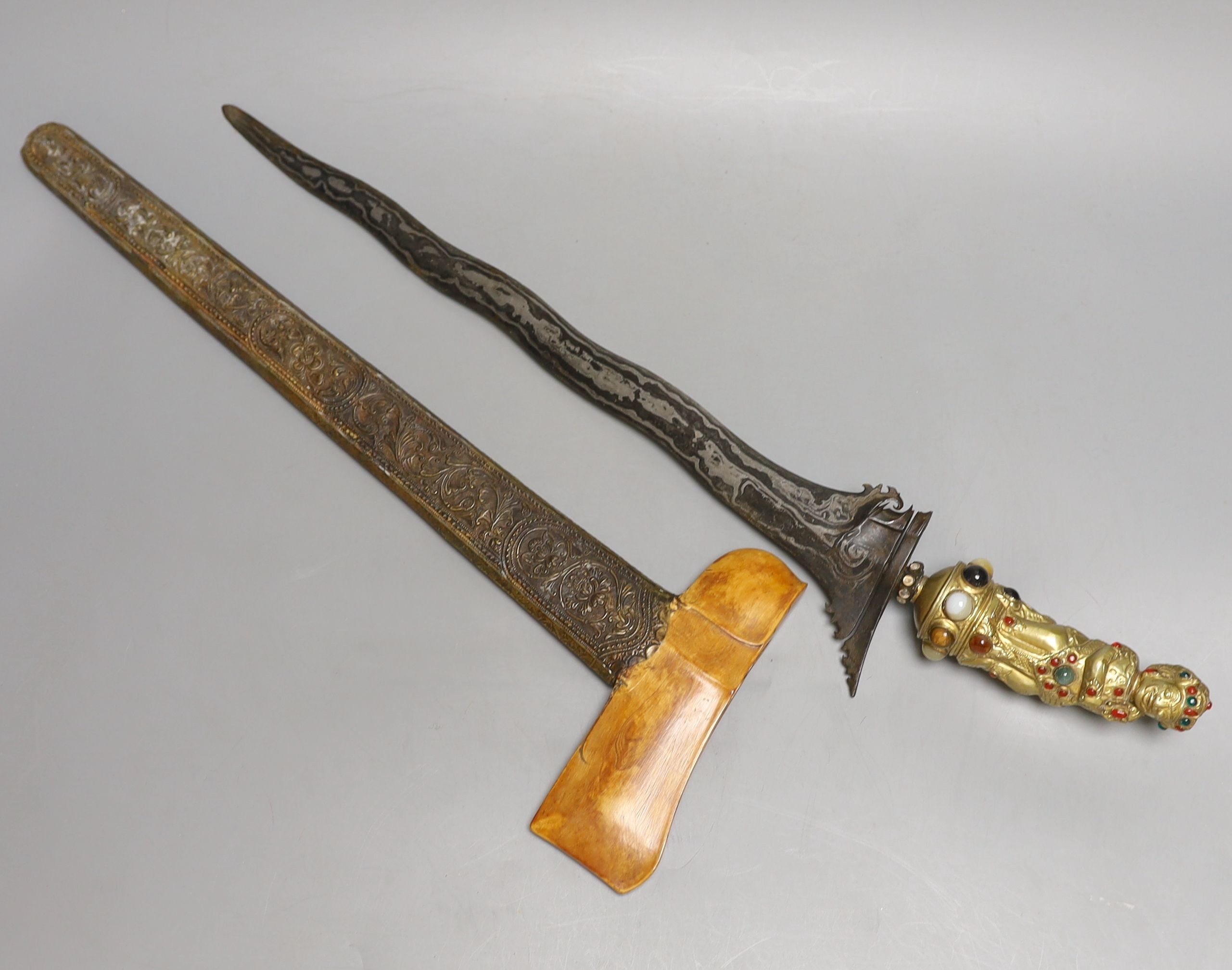 A Fine Balinese dagger kris, 19th century, earlier wavy pamor blade 43cms, later gilt brass figural handle set with cabochon stones and pastes, in its scabbard with embossed brass cover and earlier carved ivory top.